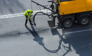 Road surface restoration work. The worker performs on road patcher work on the repair of cracks by filling and sealing with coated by bitumen emulsion and dry aggregate in the asphalt surface.